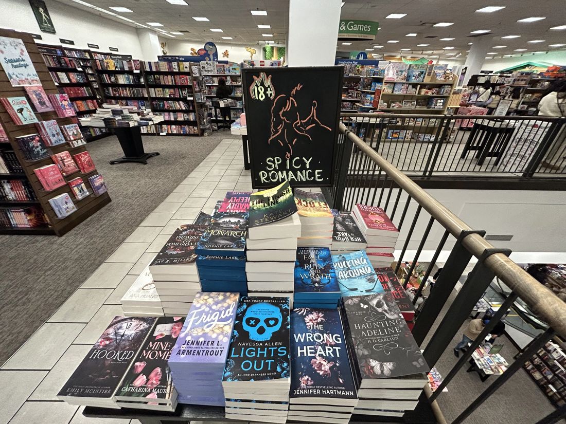 A bookstore display table stacked with dark-romance paperbacks under a sign reading Spicy Romance, 18 and up